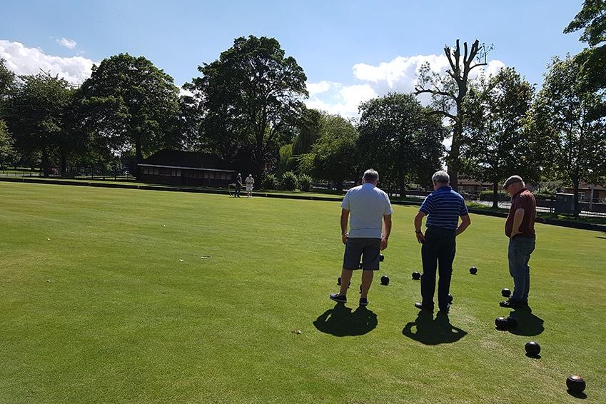 An image of 3 people playing bowls