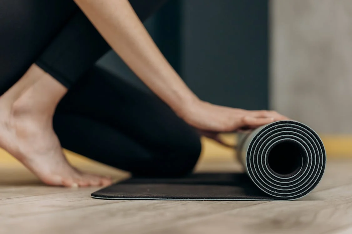 A close up photograph of a woman unrolling a Yoga mat.